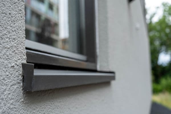 Antraciet aluminium vensterbank met kopschot, close-up op een crepi-gevel