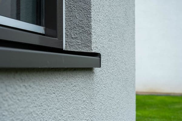 Antraciet aluminium vensterbank met zijkapjes onder een raam in een gestucte crepi-gevel