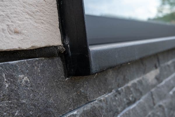 Zwarte aluminium vensterbank met zijkapje op een gevel in natuursteen