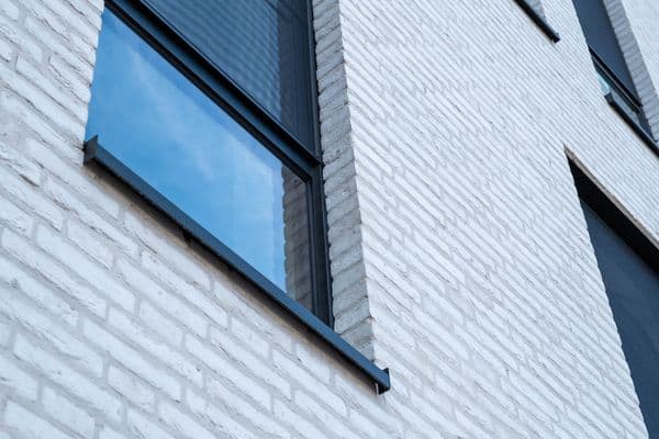 Antraciet aluminium vensterbank onder een raam in een witte baksteengevel